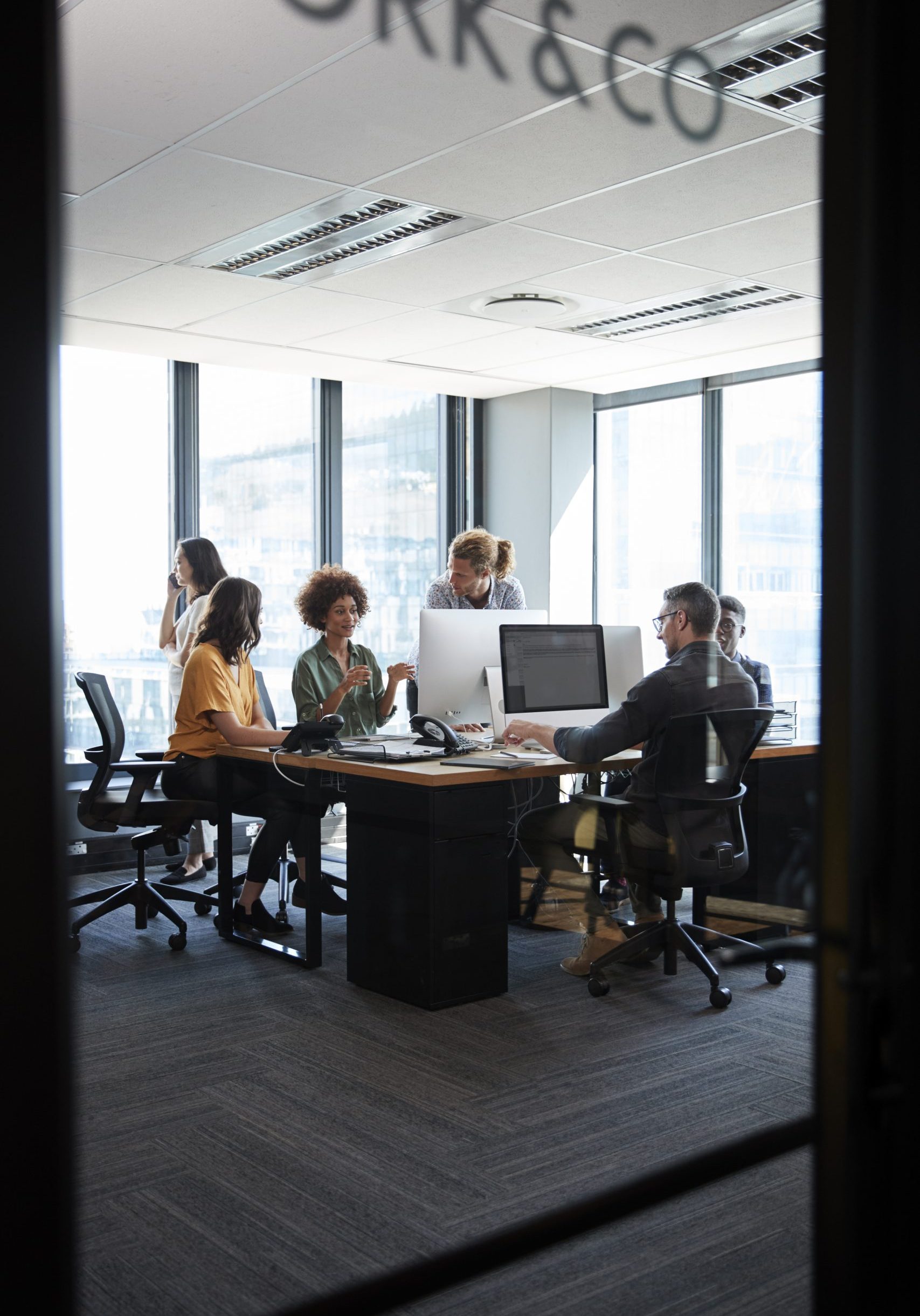 Creative business team working in a casual office, seen through glass wall with text on it, vertical