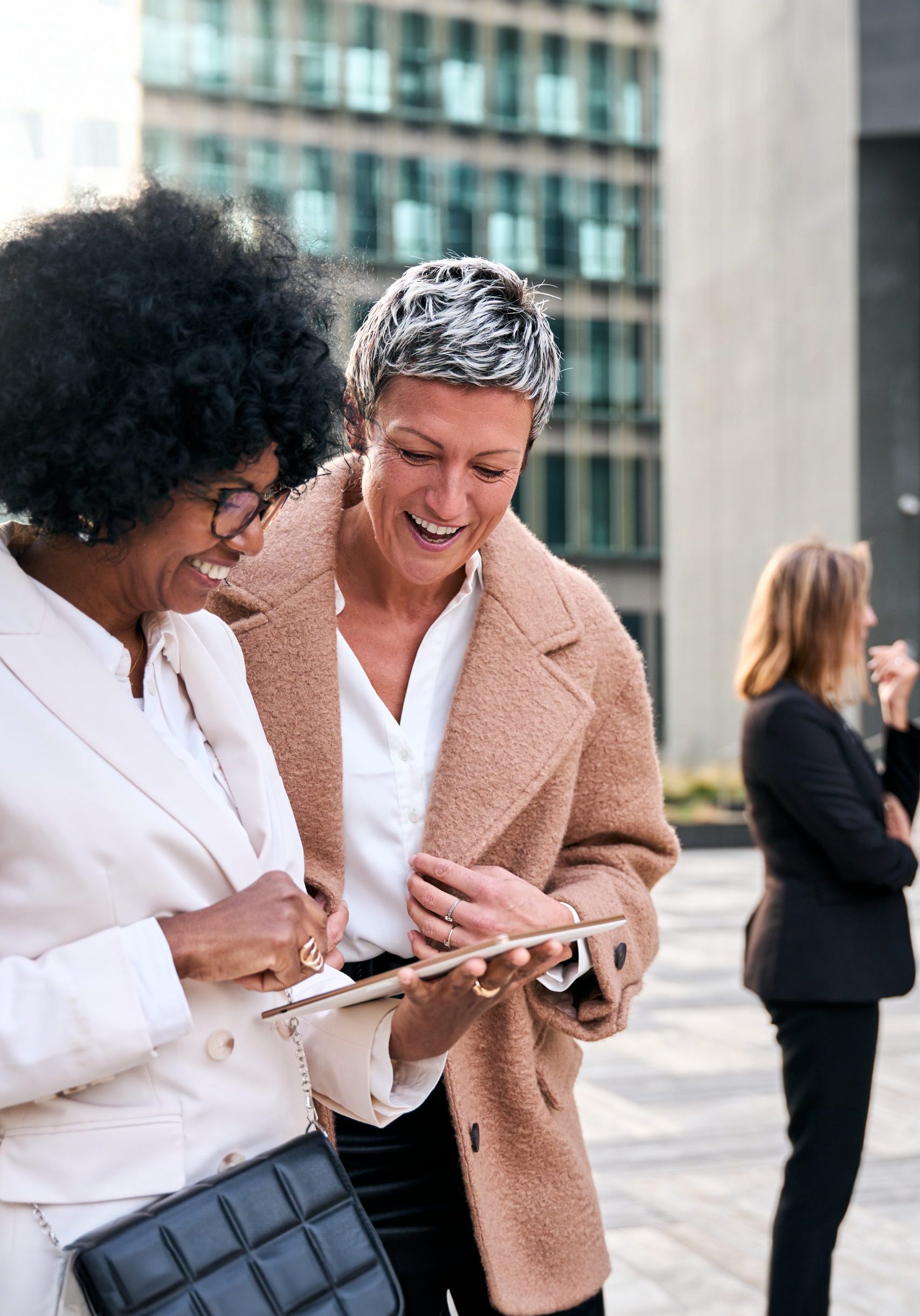 Vertical. Multiracial mature business women couple gathered looking smiling at tablet, sharing work break. Video captures expressions and reactions of professional female watching at screen together